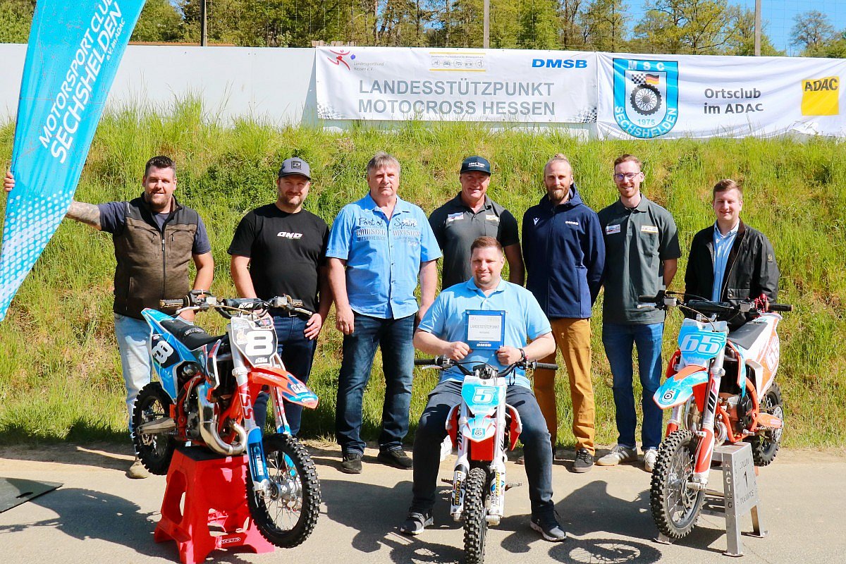 MSC Sechshelden Landessützpunkt Eröffnung 2026 Gruppe von Personen vor dem Banner „Landesstützpunkt Motocross Hessen“ beim MSC Sechshelden, mit drei Motocross-Motorrädern im Vordergrund.