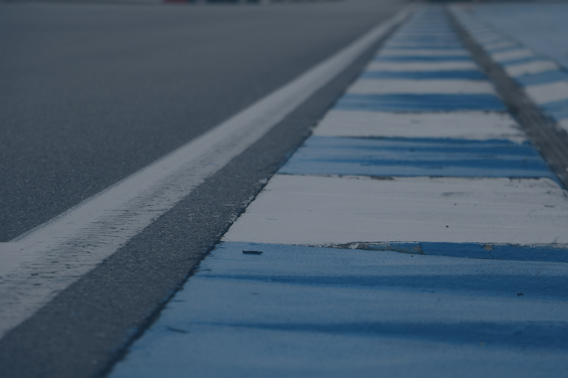 Nahaufnahme eines mit blauen und weißen Streifen bemalten Bordsteins neben der Asphaltbahn der Rennstrecke.