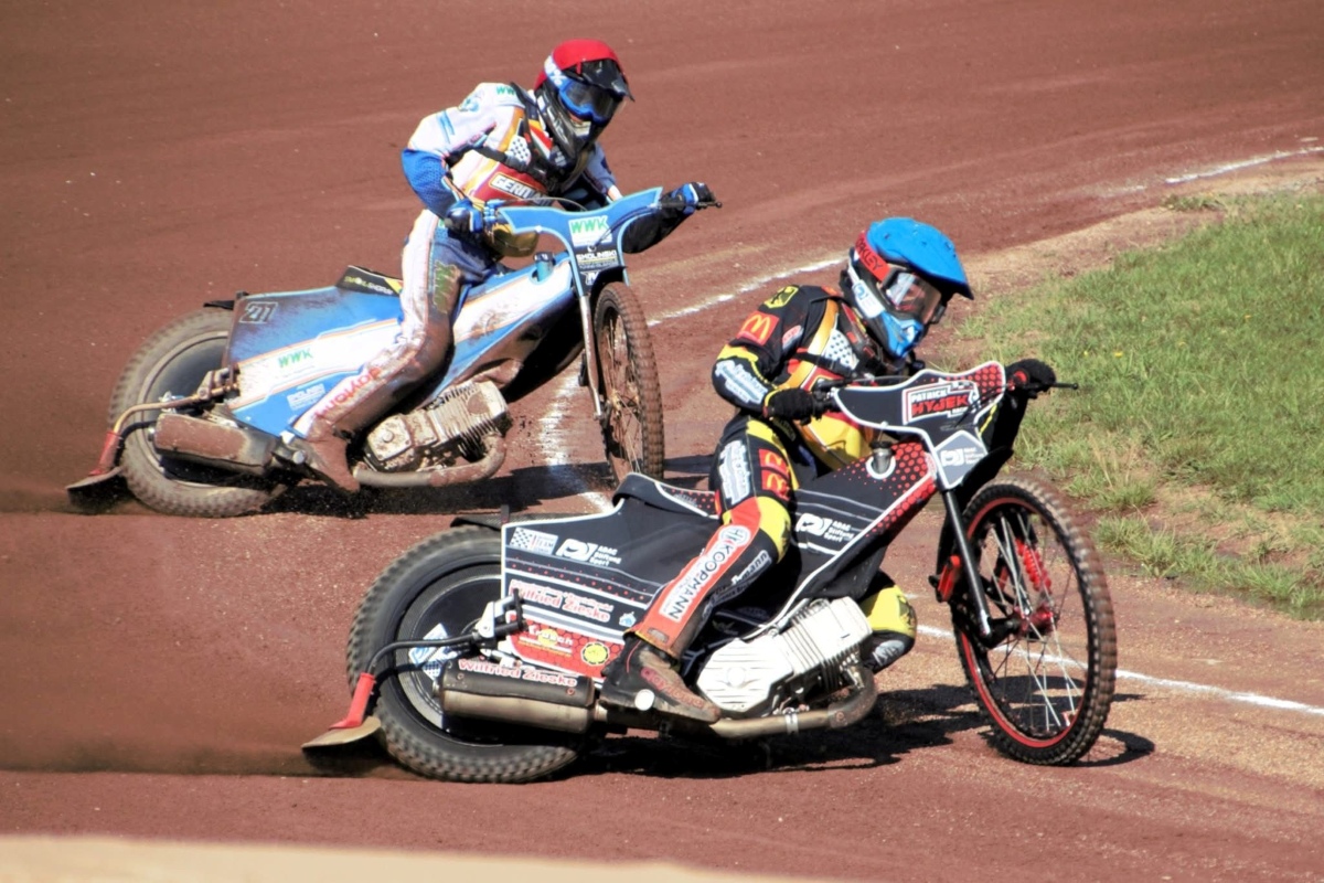 Patrick Hyjek (blauer Helm) führt Deutschland in das U19 Europafinale Zwei Speedway-Fahrer driften auf einer Sandbahn durch eine Kurve.